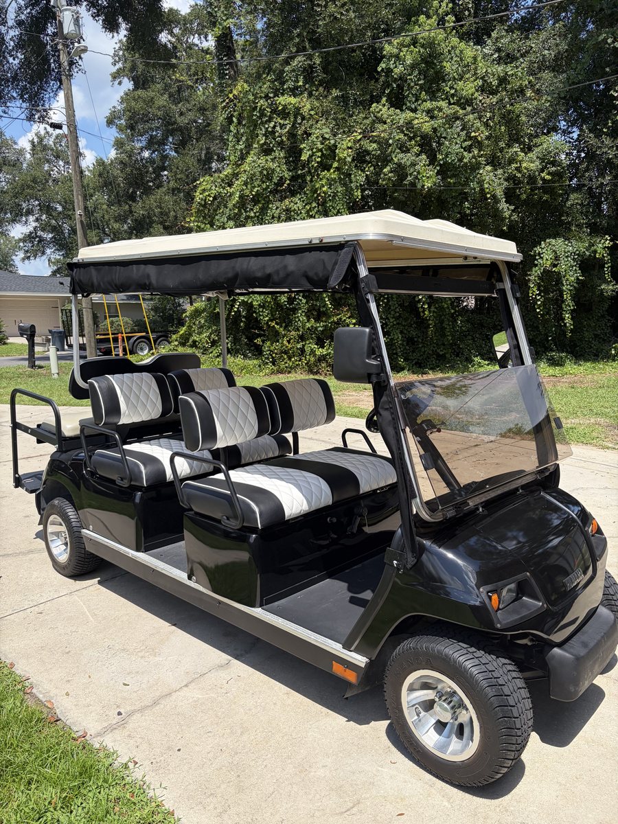 Black 6-passenger golf cart in a 4+2 layout - two forward-facing rows with black and white diamond-stitched seats, plus a rear-facing flip seat with a grab bar and footrest